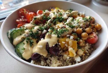 A vibrant Mediterranean Quinoa Bowl topped with chickpeas, cucumbers, tomatoes, feta, and drizzled with lemon tahini sauce.