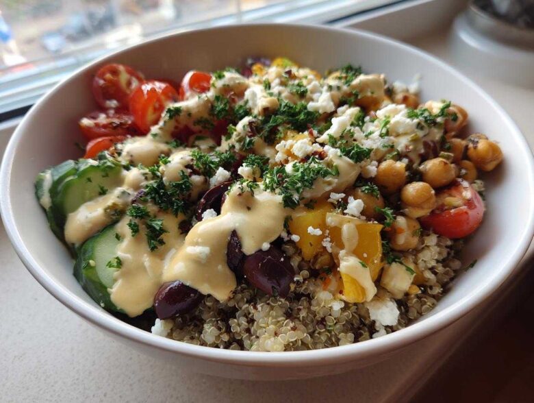 A vibrant Mediterranean Quinoa Bowl topped with chickpeas, cucumbers, tomatoes, feta, and drizzled with lemon tahini sauce.