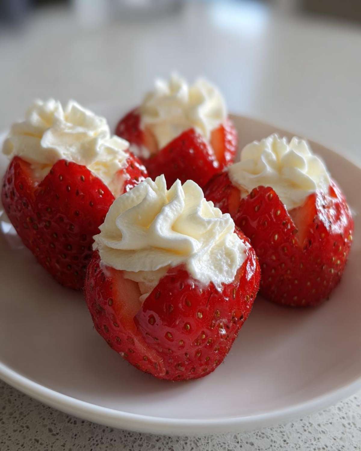 Four vibrant red No-Bake Cheesecake Stuffed Strawberries topped with piped cream cheese filling on a white plate.