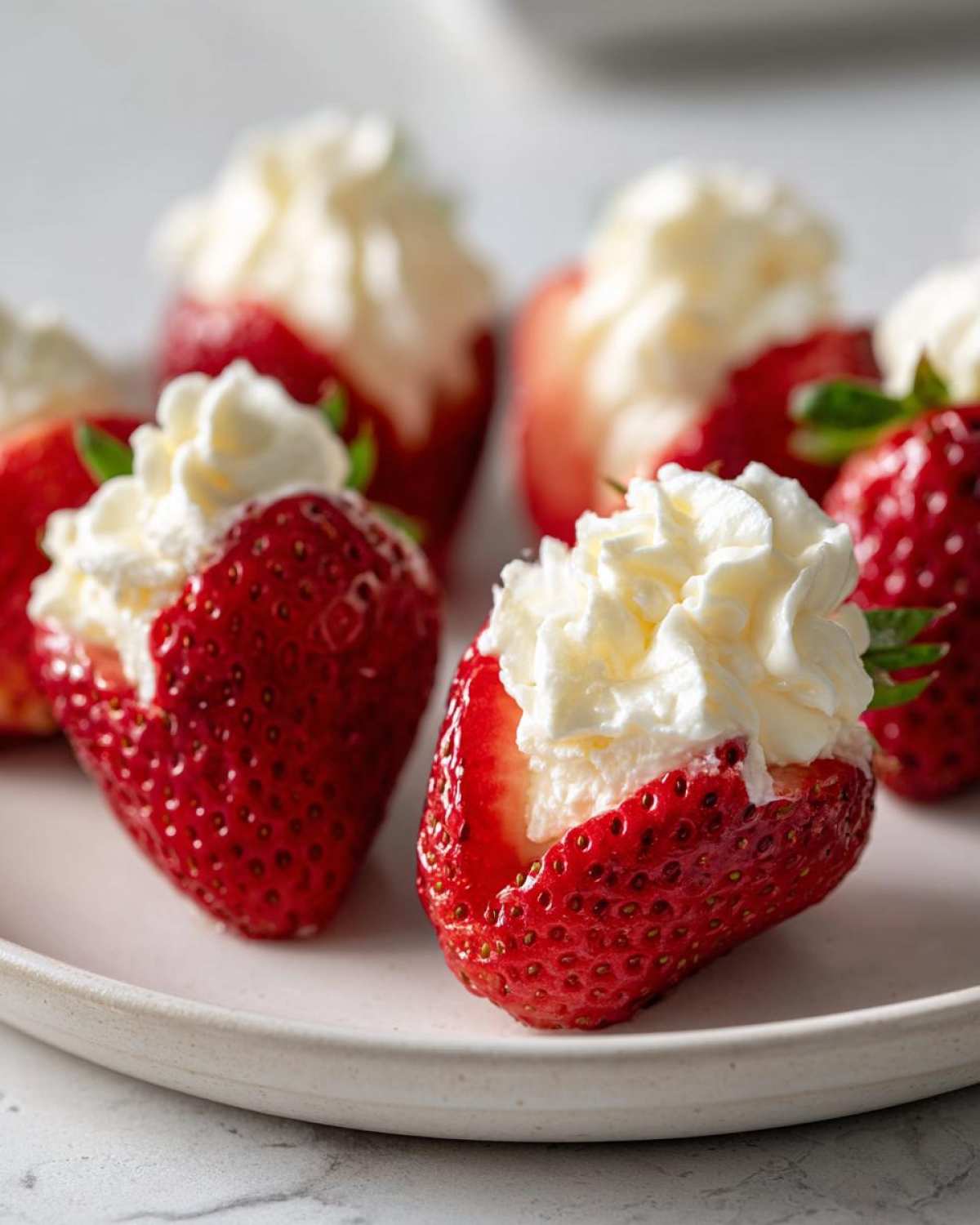 Close-up of bright red strawberries hollowed out and filled with creamy white no-bake cheesecake filling.