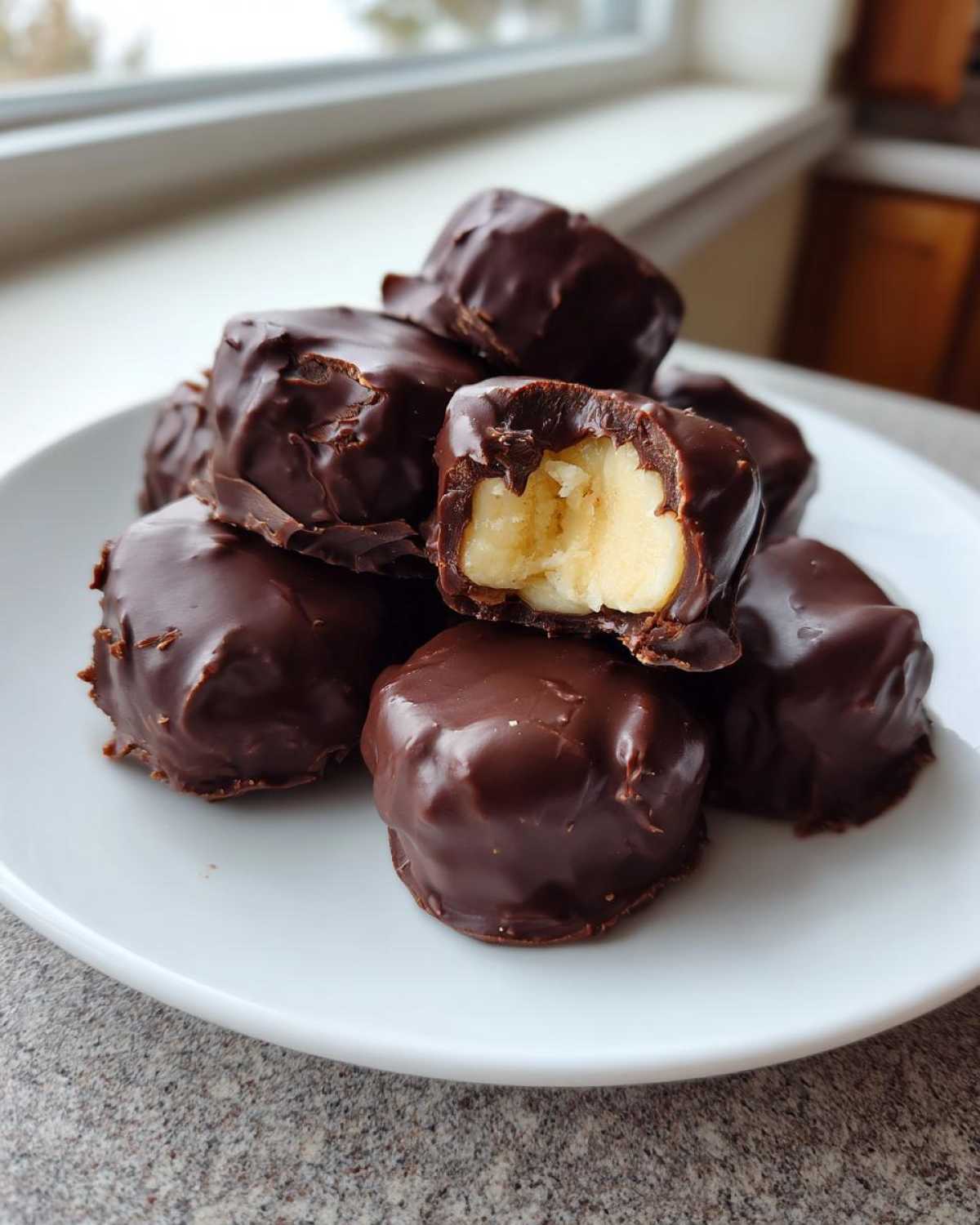 A stack of rich, dark chocolate covered banana bites, with one piece broken open to show the creamy banana filling.