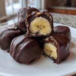 A stack of No-Bake Chocolate Covered Banana Bites on a white plate, with two pieces cut open showing the banana center.
