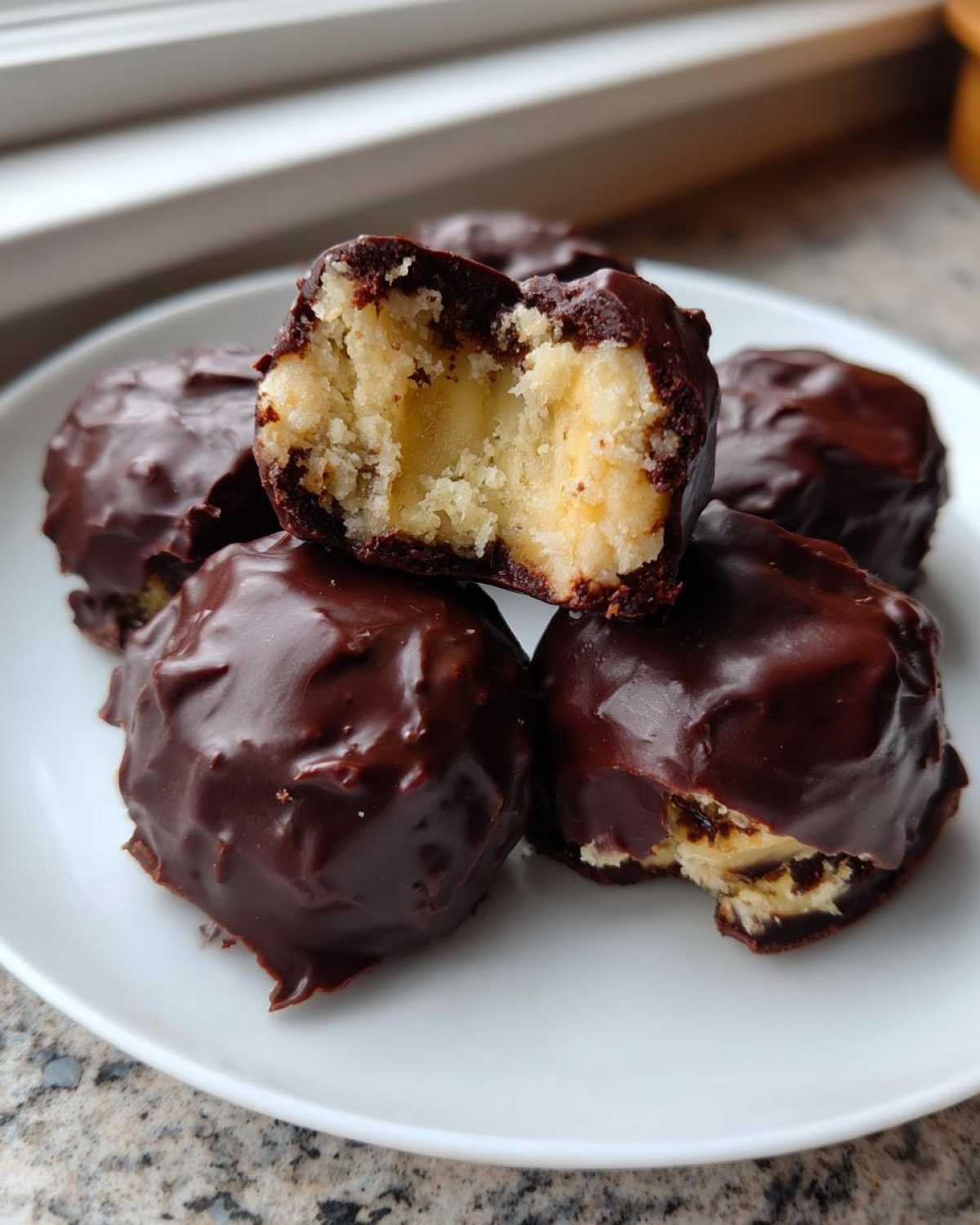 A stack of rich, dark chocolate covered banana bites, one bitten into revealing the creamy yellow interior.