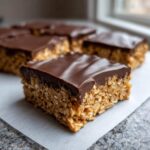 A close-up of a square No-Bake Chocolate Peanut Butter Oat Bars showing the thick oat base and smooth chocolate topping.