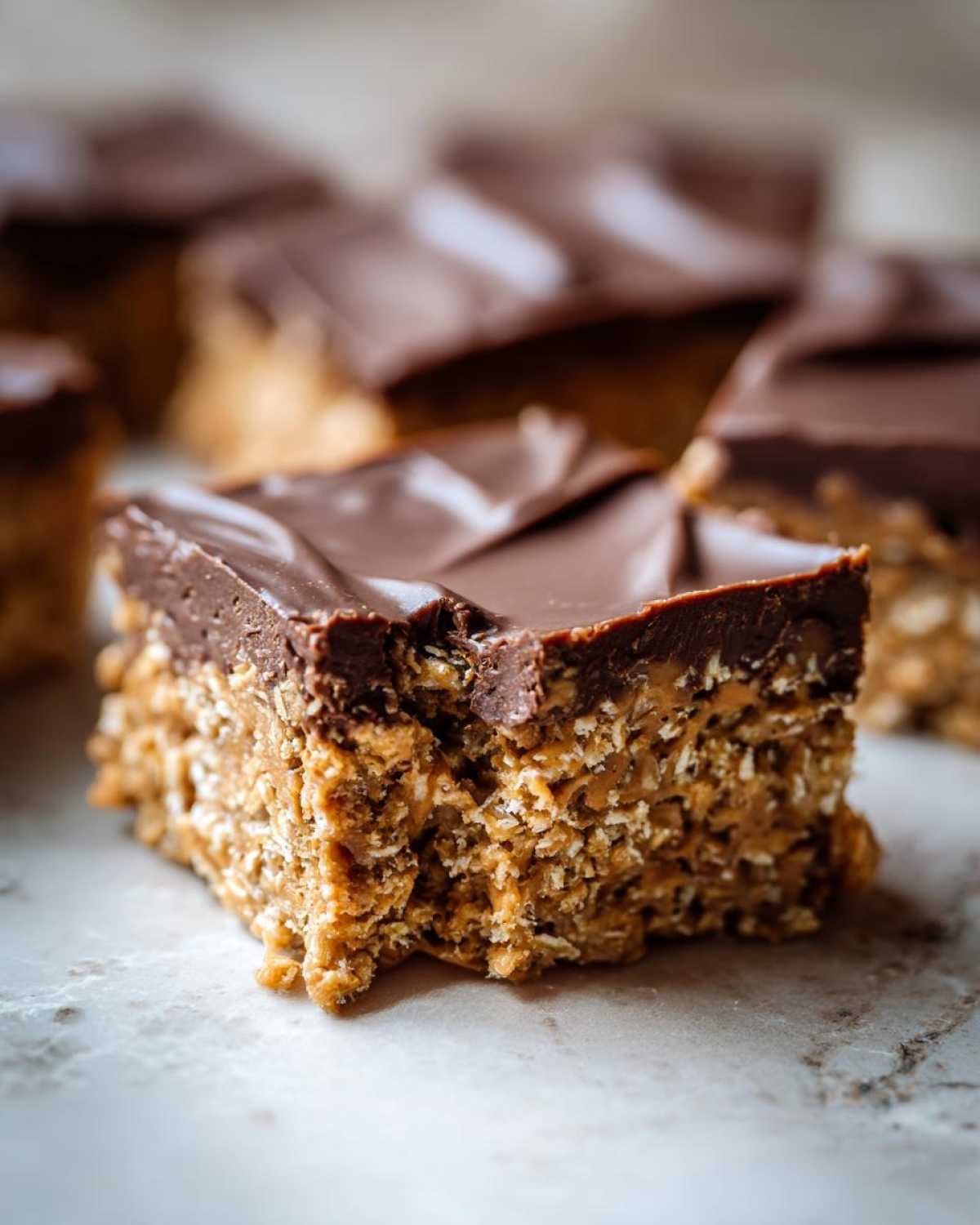A close-up of a rich, square piece of No-Bake Chocolate Peanut Butter Oat Bars showing the textured oat base and smooth chocolate topping.