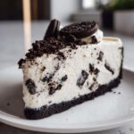 A close-up of a creamy slice of No-Bake Oreo Cheesecake with chunks of cookie mixed in and topped with crumbs.