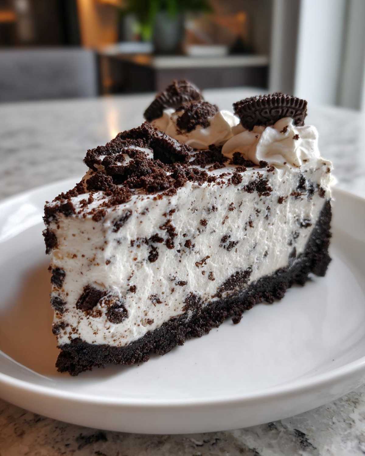 A decadent slice of No-Bake Oreo Cheesecake on a white plate, topped with whipped cream and cookie pieces.