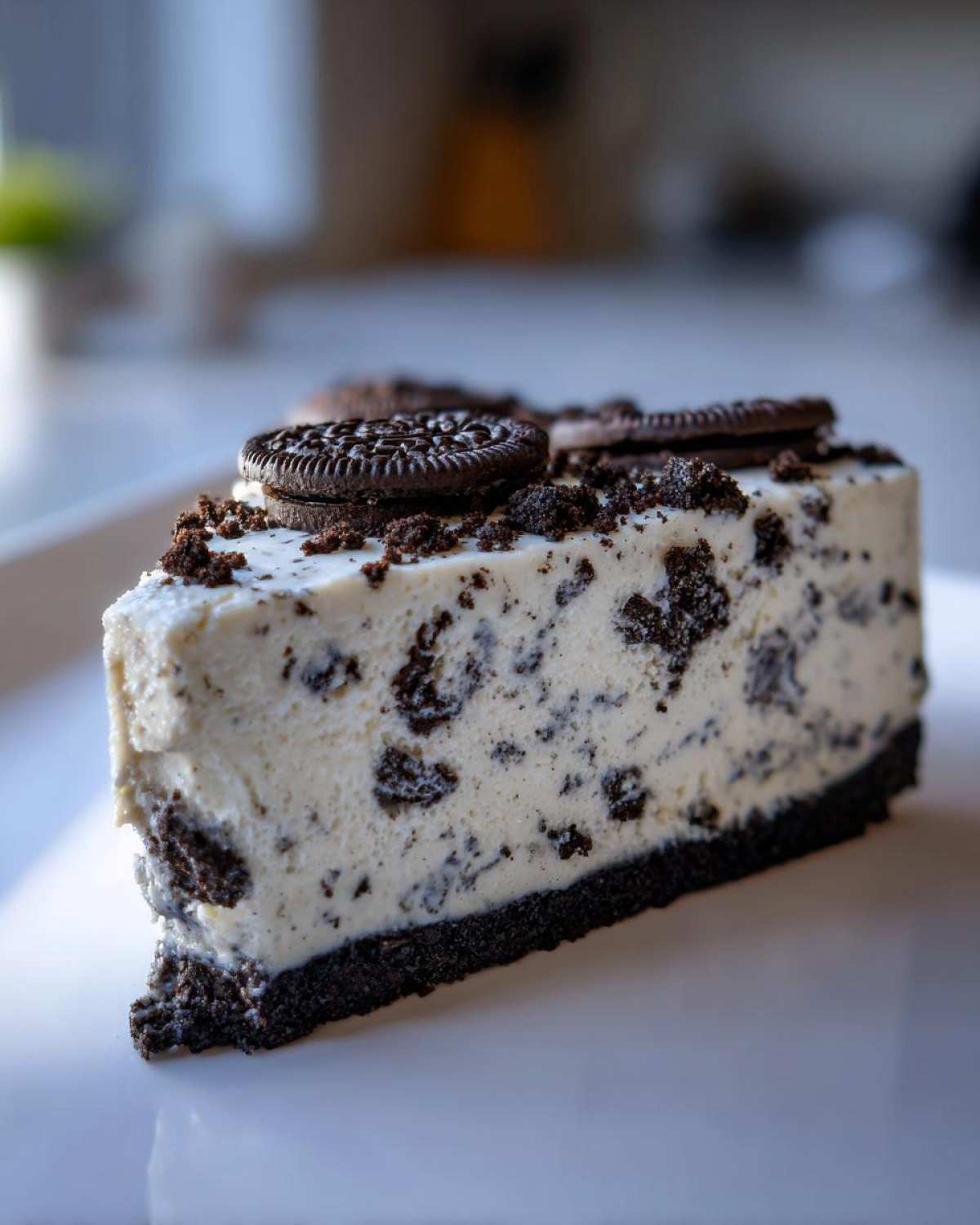 A close-up, tempting slice of No-Bake Oreo Cheesecake featuring a creamy filling loaded with cookie pieces and topped with whole Oreos.
