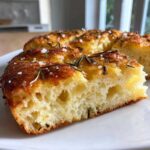 A thick slice of No-Knead Skillet Focaccia showing its airy interior, topped with rosemary and coarse salt.