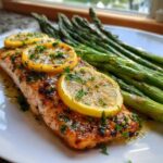 A perfectly cooked fillet of One-Pan Lemon Garlic Salmon with asparagus spears, topped with lemon slices and parsley.