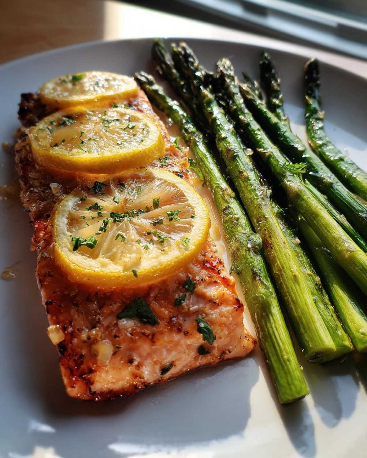 A perfectly cooked fillet of One-Pan Lemon Garlic Salmon with asparagus spears, topped with lemon slices.