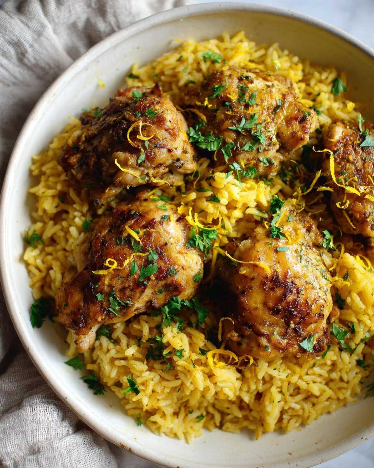 Close-up of golden One-Pot Chicken and Rice with Lemon and Herbs, topped with zest and parsley.