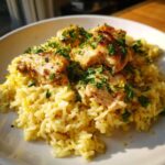 A close-up of One-Pot Chicken and Rice with Lemon and Herbs, topped with browned chicken pieces and fresh parsley.