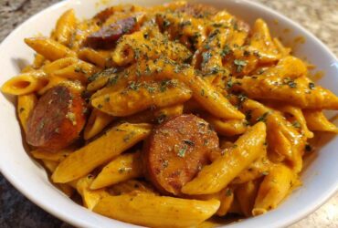 A white bowl filled with One-Pot Creamy Cajun Sausage Pasta, featuring penne coated in orange sauce and sliced sausage.