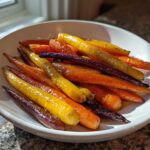 A white bowl filled with glossy, roasted Sheet Pan Roasted Rainbow Carrots with Honey in orange, yellow, and purple.