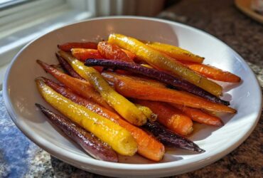 A white bowl filled with glossy, roasted Sheet Pan Roasted Rainbow Carrots with Honey in orange, yellow, and purple.