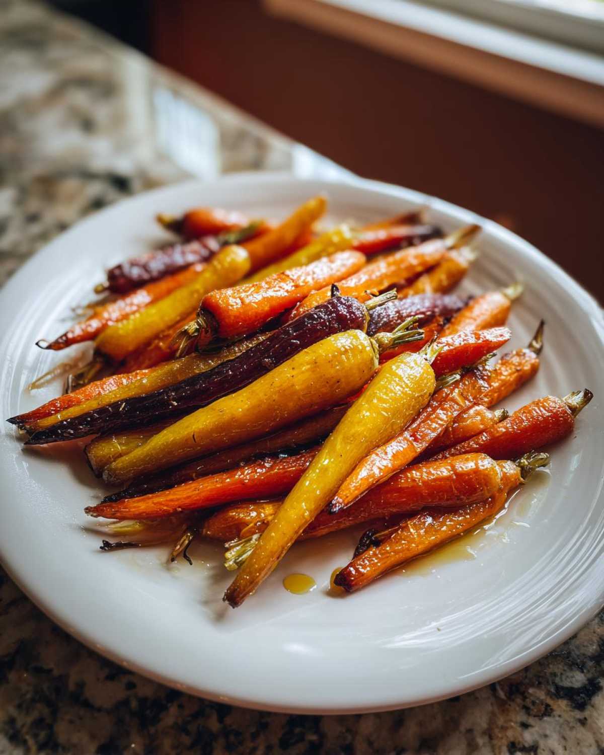 A close-up of glazed Sheet Pan Roasted Rainbow Carrots with Honey piled on a white plate.