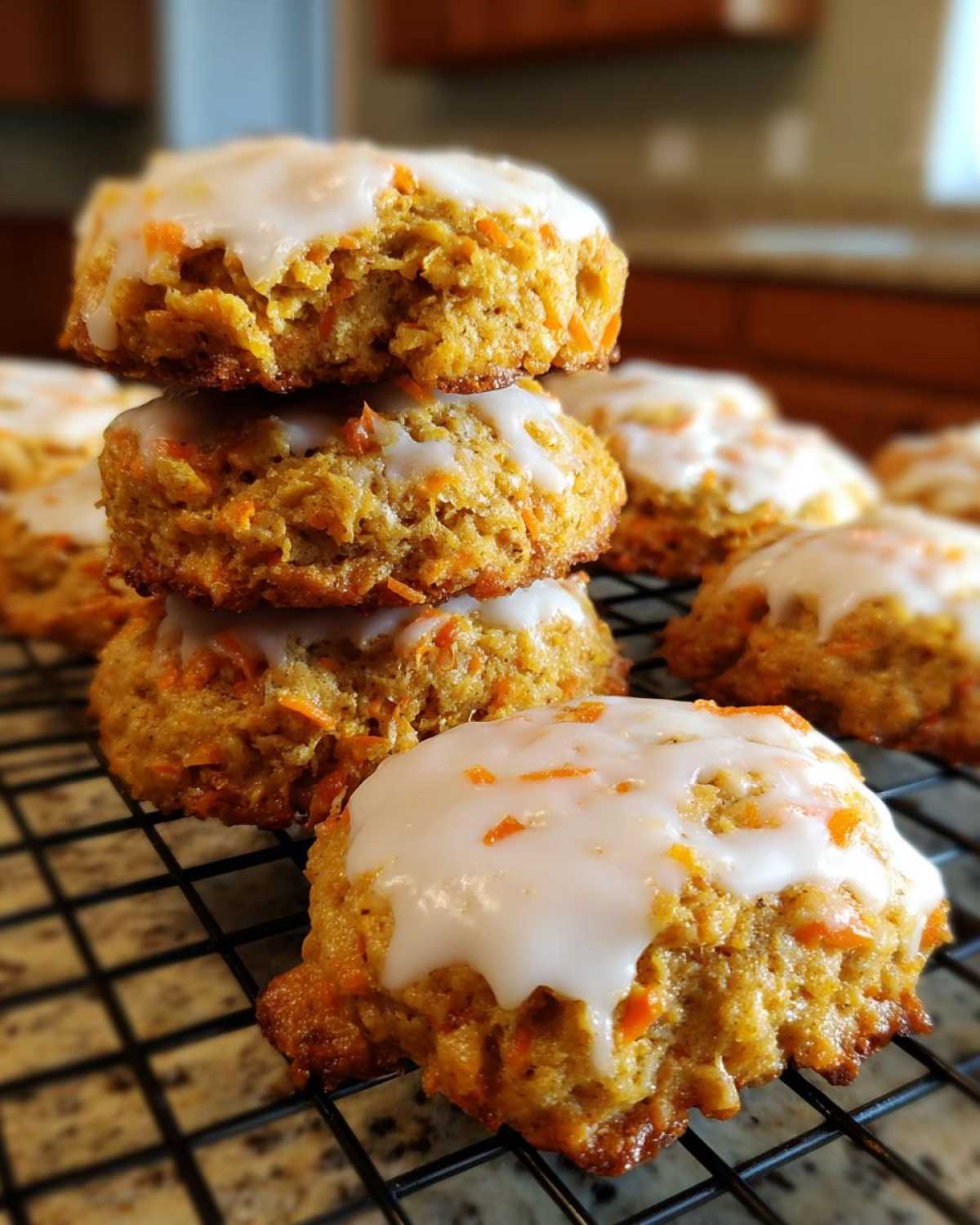A stack of Soft-Baked Carrot Cake Cookies topped with a thick cream cheese glaze cooling on a wire rack.