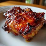 Close-up of a perfectly cooked, glazed Spicy Honey Garlic Air Fryer Chicken Thighs piece on a white plate.