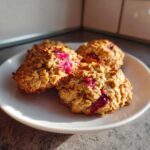 Four freshly baked Strawberry Oatmeal Breakfast Cookies with visible oats and bright pink strawberry pieces, served on a white plate.