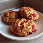 Three golden brown Strawberry Oatmeal Breakfast Cookies studded with bright red fruit pieces, served on a small white plate.