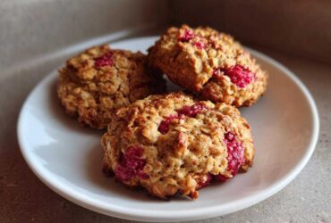 Three golden brown Strawberry Oatmeal Breakfast Cookies studded with bright red fruit pieces, served on a small white plate.