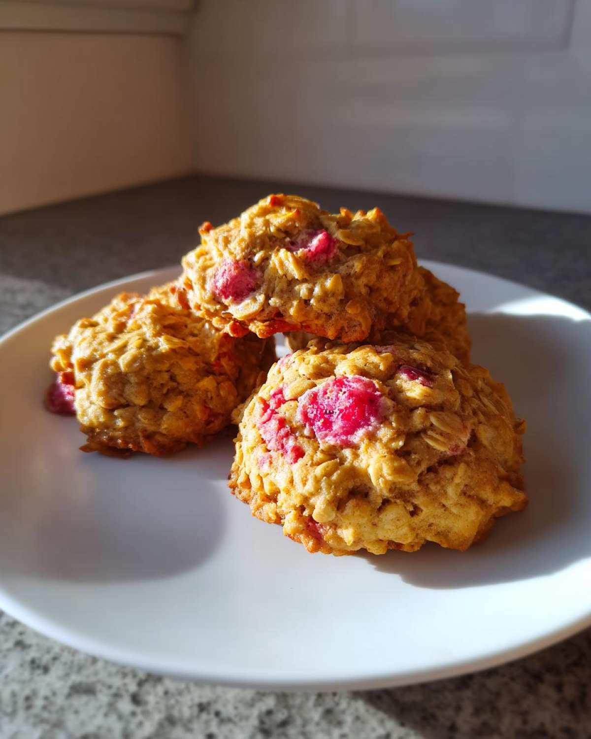 A stack of four golden Strawberry Oatmeal Breakfast Cookies with visible chunks of bright pink strawberries.