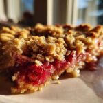 A close-up, sunlit slice of Strawberry Rhubarb Crisp showing bright red fruit filling and crunchy topping.