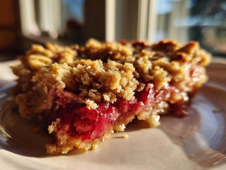A close-up, sunlit slice of Strawberry Rhubarb Crisp showing bright red fruit filling and crunchy topping.