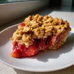 A close-up slice of Strawberry Rhubarb Crisp showing the bright red fruit filling and golden brown oat topping.