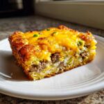 A golden brown slice of Tater Tot Breakfast Casserole topped with melted cheddar cheese and green onions.