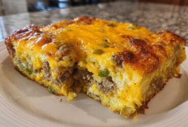 A close-up slice of Tater Tot Breakfast Casserole topped with melted cheddar cheese and sausage.