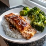 A fillet of glazed Teriyaki Salmon served over white rice with steamed broccoli florets, sprinkled with sesame seeds.
