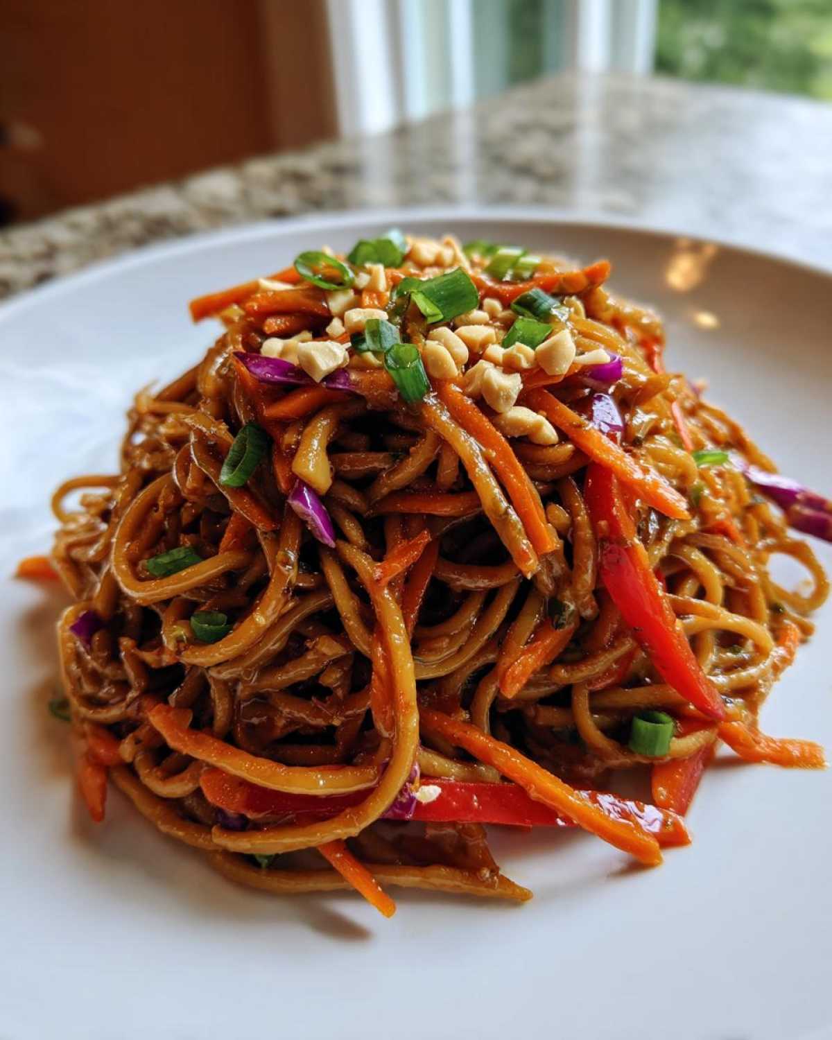 A mound of glossy Thai Peanut Noodles with crunchy shredded carrots, red peppers, and topped with chopped peanuts and green onions.