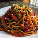 A close-up of a mound of Thai Peanut Noodles with Crunchy Veggies, topped with peanuts and green onions.