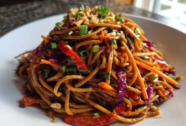 A close-up of a mound of Thai Peanut Noodles with Crunchy Veggies, topped with peanuts and green onions.