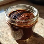 Close-up of thick Vegan Chocolate Chia Pudding set in a small glass jar, catching sunlight.