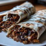Two halves of a Vegan Mushroom Shawarma wrap, generously filled with spiced mushrooms and drizzled with white sauce, served on a white plate.