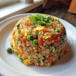 A dome-shaped serving of Vegetable Fried Rice with peas, carrots, and egg, topped with green onions.