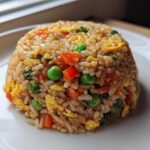 A perfectly molded dome of colorful Vegetable Fried Rice with peas, carrots, and scrambled egg on a white plate.