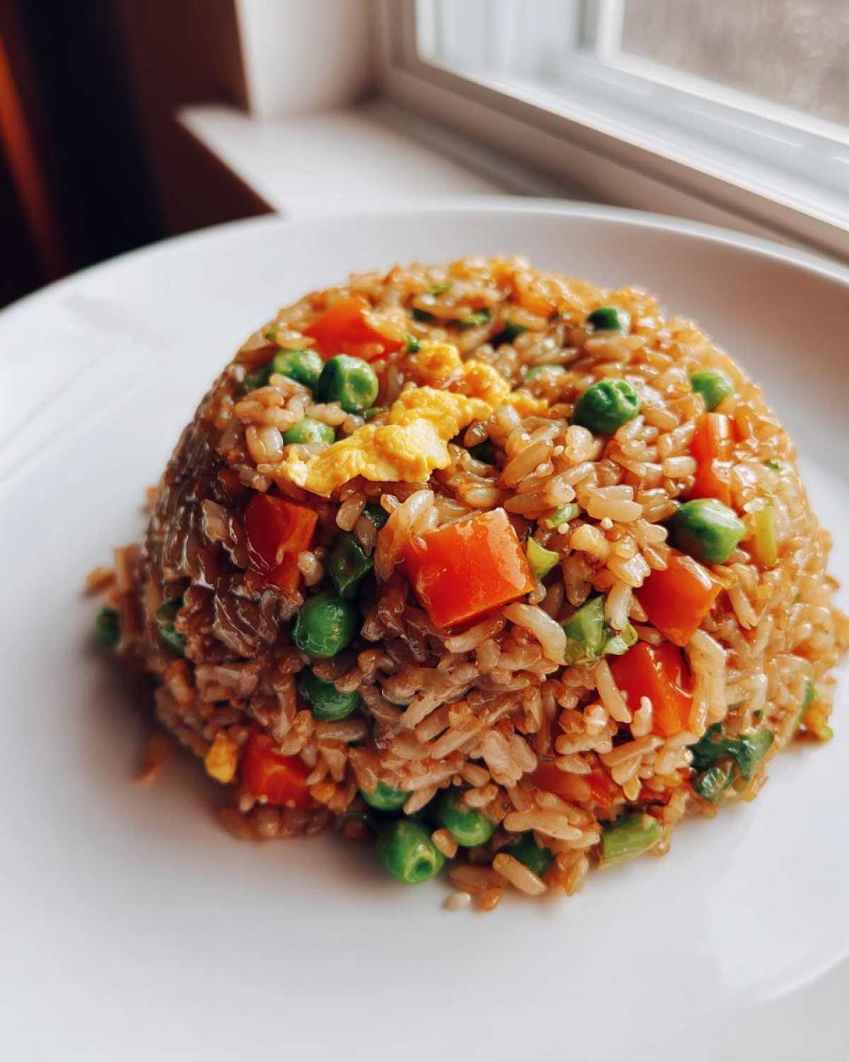 A perfectly molded mound of Vegetable Fried Rice with peas, diced carrots, and scrambled egg on a white plate.