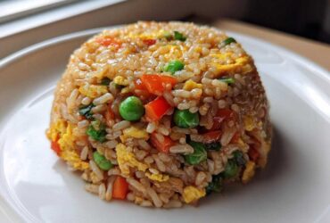 A perfectly molded dome of colorful Vegetable Fried Rice with peas, carrots, and scrambled egg on a white plate.