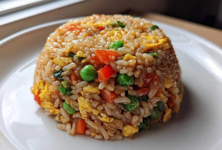 A perfectly molded dome of colorful Vegetable Fried Rice with peas, carrots, and scrambled egg on a white plate.