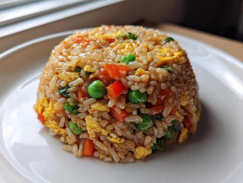 A perfectly molded dome of colorful Vegetable Fried Rice with peas, carrots, and scrambled egg on a white plate.