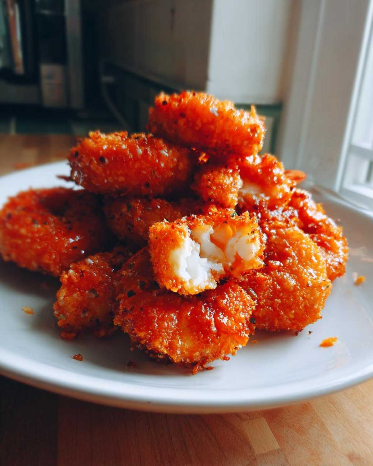 A pile of bright orange, crispy Air Fryer Crispy Buffalo Shrimp stacked on a white plate, with one piece broken open showing the white shrimp meat.