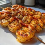Close-up of several Air Fryer Crispy Cajun Shrimp Skewers arranged on a white plate, glistening with seasoning.