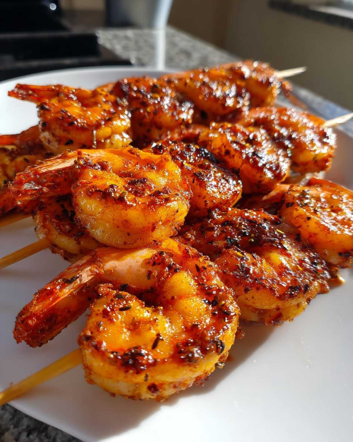 Close-up of several Air Fryer Crispy Cajun Shrimp Skewers piled on a white plate, showing their vibrant orange color and seasoning.