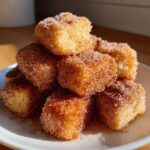 A stack of golden Air Fryer Crispy Cinnamon French Toast Bites coated heavily in cinnamon sugar on a white plate.