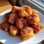 A pile of golden Air Fryer Crispy Cinnamon Sugar Biscuit Bites coated heavily in sparkling cinnamon sugar on a white plate.