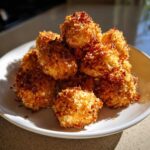 A pile of golden brown, crispy Air Fryer Crispy Coconut Chicken Bites stacked on a white plate.
